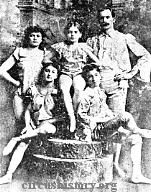 Black and white photo with two children seated, mother standing to the left, one child standing in the middle, and father standing to the right.