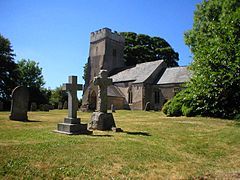 Stone building with square tower. In the foreground are stone crosses, gravestones and trees.