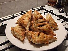 Six puff pastry triangles filled with mincemeat on a plate, each with three slits scored in them