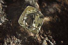 A clear octahedral stone protrudes from a black rock