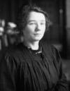 a black and white photograph of a young woman in a black smock