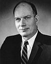 Black-and-white photo of a balding man in a suit and striped tie