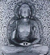 Front view of a cross-legged seated statue, showing the meditation gesture (Dhyāna Mudrā) with both hands placed on the lap, palms facing upwards. Black and white picture.