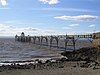 Metal pier standing on thin legs rising from the sea. Beach in the foreground