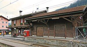 Two-story building with gabled roof and adjoining single-story wooden shed