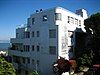 A white and silver apartment building with streamlined curves, perched on a hillside overlooking a bay and bridge