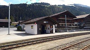 Shelter next to double-track railway line with mountain behind and chalet-style buildings to the right