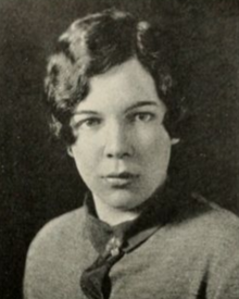 A young white woman with dark wavy hair parted on the side and cut into a short bob, wearing a knit top with a darker collar and front placket