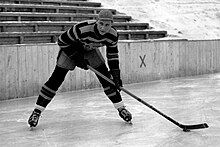 Black and white photo of a hockey place on ice, holding a stick and wearing a hat