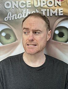 Riley in front of a poster of his cover to ONCE UPON ANOTHER TIME in 2022.