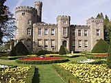 Victorian castellated mansion with a keep to the left and formal gardens in the foreground