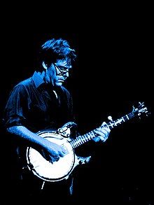 bespectacled man in shirtsleeves playing banjo