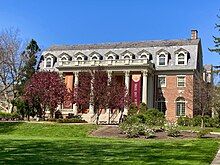 Two-and-a-half-story red-brick building with a large porch with six Roman Doric columns and orange and maroon banners on each end