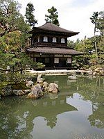 A two-storied wooden building with white walls in the lower part, wooden walls in the upper part and a pyramid shaped roof.