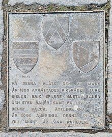 A metal plate with three coats of arms arranged in a triangular formation above a short Swedish text