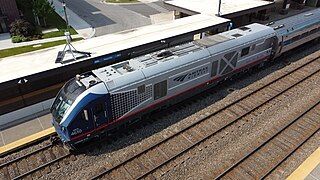 Gray diesel locomotive with a red sill stripe. The area around the cab windows is black. The sides of the cab are blue, tapering with halftone dots onto the side of the body.