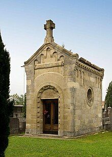 A small stone building topped by a cross, in a cemetery.