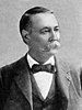 A white man with a full mustache in a dark suit with a bow tie and vest, looking right.