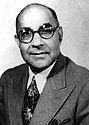 A black and white headshoot of a man wearing spectacles