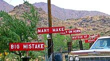 A set of 6 white-on-red signs with white block text along the side of a road, reading in order "BIG MISTAKE", "MANY MAKE", "RELY ON HORN", "INSTEAD OF BRAKE", and, stylized, "Burma-Shave".