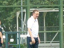 A man with short brown hair in a white shirt and black pants