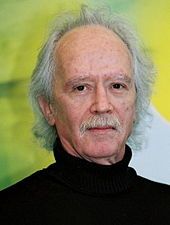 An elderly Caucasian man with a gray mustache and gray receding hair faces the camera with a neutral expression.