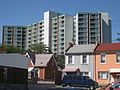 High rise aprtment building with a geometric design, positioned just behind two storey high attached and detached houses.