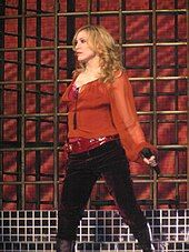 A blonde woman wearing a red shirt and dark pants is performing