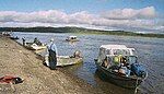 Men and boats along the shore of a very wide river.