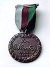 Bronze medal encircled in a laurel wreath and inscribed "PDSA For Gallantry We Also Serve" held from a ring suspender by a ribbon consisting of three equal vertical stripes of dark green, brown and pale blue.