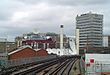 A series of white satellite dishes on the roofs of buildings with a railway track in the foreground all under a light blue sky with white clouds