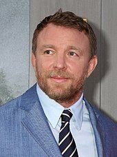 Guy Ritchie in a blue coat looking to the right.