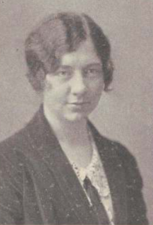 A young white woman with wavy hair cut in a short bob with a sidepart; she is wearing a dark jacket over a light-colored blouse.