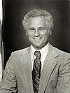 Black-and-white photo of a man with a wide smile and short curly hair wearing a light-colored suit