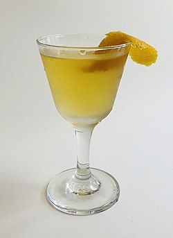 A deep yellow cocktail in a cocktail glass, garnished with an orange peel.