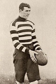 A dark-haired footballer in a long-sleeve horizontally-striped guernsey holding a football