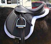 An English saddle set on top of a white pad that has the same shape as the saddle