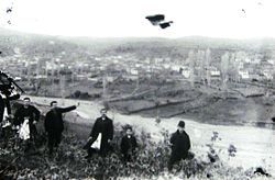 Black-and-white photo of people in the foreground, with a village hazily in the background