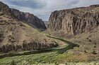 View over a river bend in a shrubby desert landscape framed by vertical cliffs