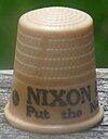 An off-white thimble, with the visible black lettering, "NIXON/Put the ne ...