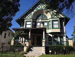 Image of a two-story, stone and stucco, green and white, Tudor Revival house in the sun