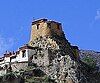 A small brown ancient tower on a hilltop next to a white house.