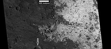 Enlargement of light-toned layer on floor of Suzhi Crater, as seen by HiRISE, under HiWish program. Arrow points to a small crater that contains the light-toned material.