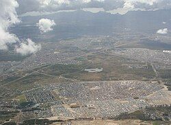 An aerial photograph of Mfuleni in the foreground stretching to the west towards Table Mountain. Ikweze Park (on the left) and Delft (to the right) are situated beyond.