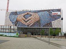 A 2013 CDU billboard near the Berlin Hauptbahnhof uses a mosaic of supporters' photographs to depict the Merkel-Raute.