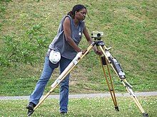 A woman setting up an optical level on a tripod.