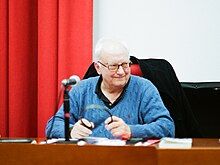 Étienne Balibar in a blue pullover sweater, at a desk with a microphone.