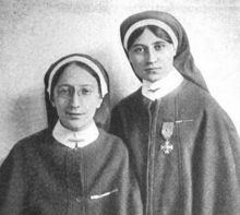 Two white women in nursing habits; the shorter woman, on left, is wearing eyeglasses; the taller woman, on right, has a medal pinned to her smock