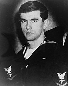 A picture of a man in a United States Navy uniform while looking at the camera with a stern face.