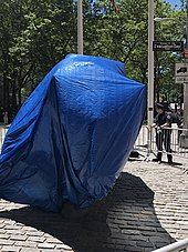 Charging Bull covered in a blue tarp and surrounded by barricades to protect it from vandalism. This photo was taken in June 2020, during the George Floyd protests in New York City.